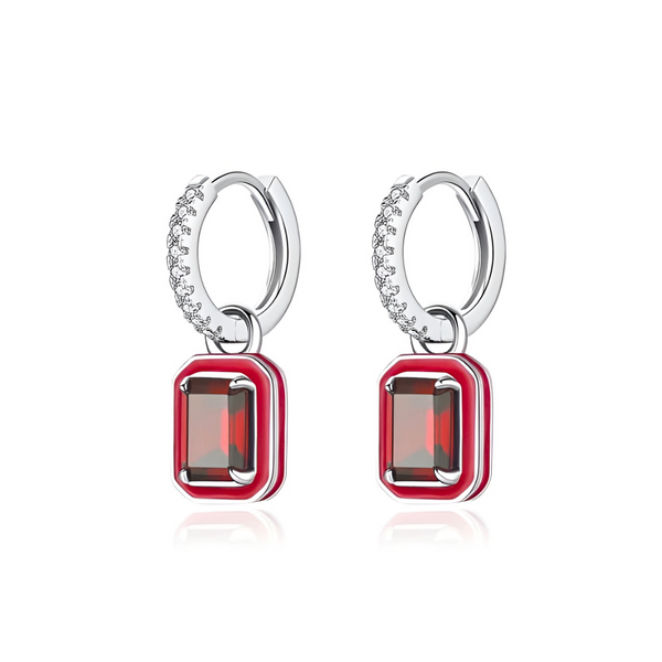 A pair of silver hoop earrings with small diamonds on the hoops and red rectangular gems encased in a red enamel border hanging from the hoops.