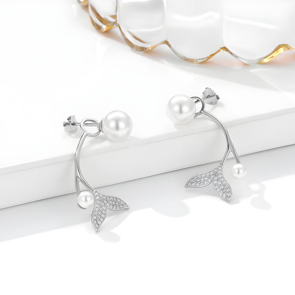 Silver hoop earrings with leaf motifs and pearls, presented on a reflective white surface beside a gold-rimmed ornament.