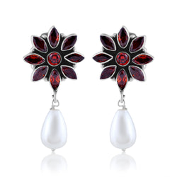 A pair of silver earrings with a flower design made of red gemstones and a dangling white pearl.