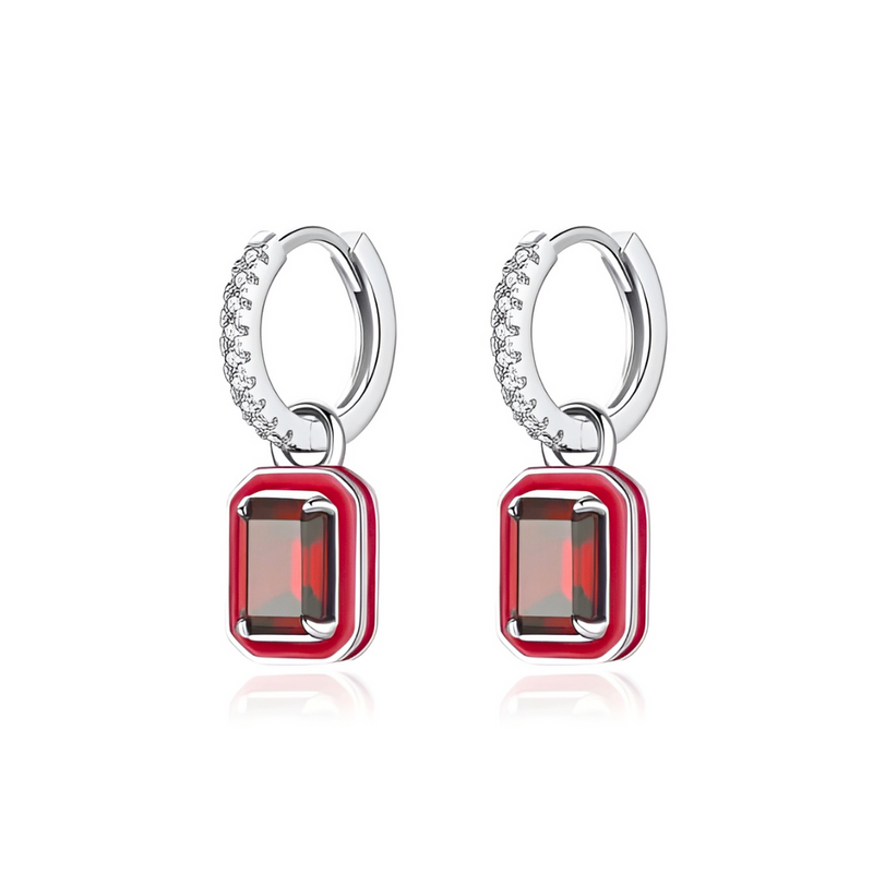 A pair of silver hoop earrings with small diamonds on the hoops and red rectangular gems encased in a red enamel border hanging from the hoops.