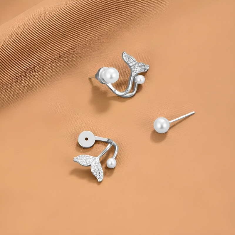 A pair of pearl earrings with diamond embellishments on a beige fabric background.