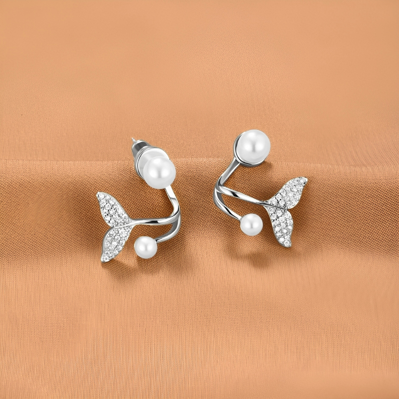 A pair of pearl earrings with diamond embellishments on a beige fabric background.