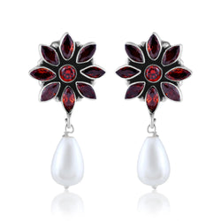 A pair of silver earrings with a flower design made of red gemstones and a dangling white pearl.